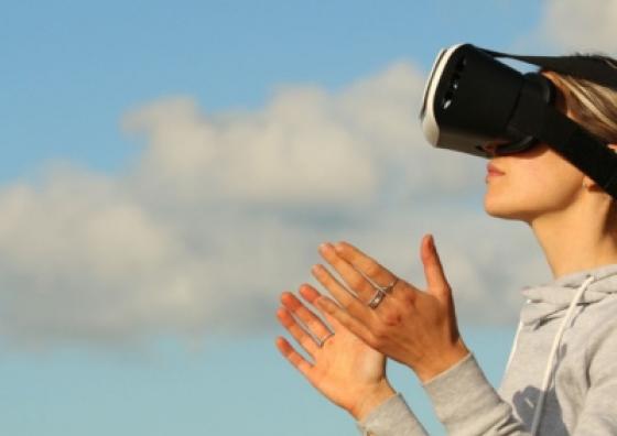 Noia amb ulleres de realitat virtual. De fons, es veu el cel i alguns núvols.